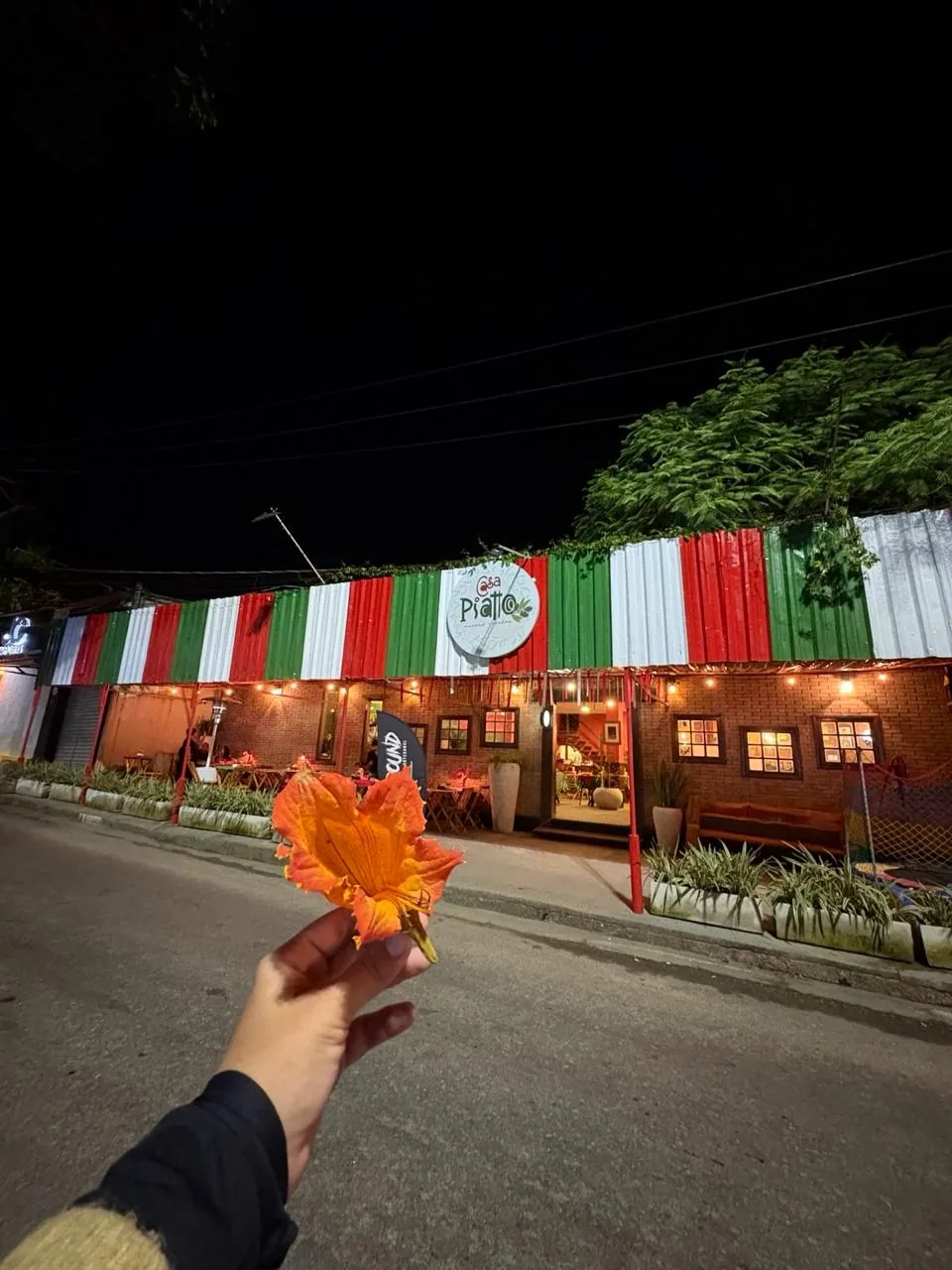 Fachada iluminada da Casa Piatto à noite com cliente na entrada