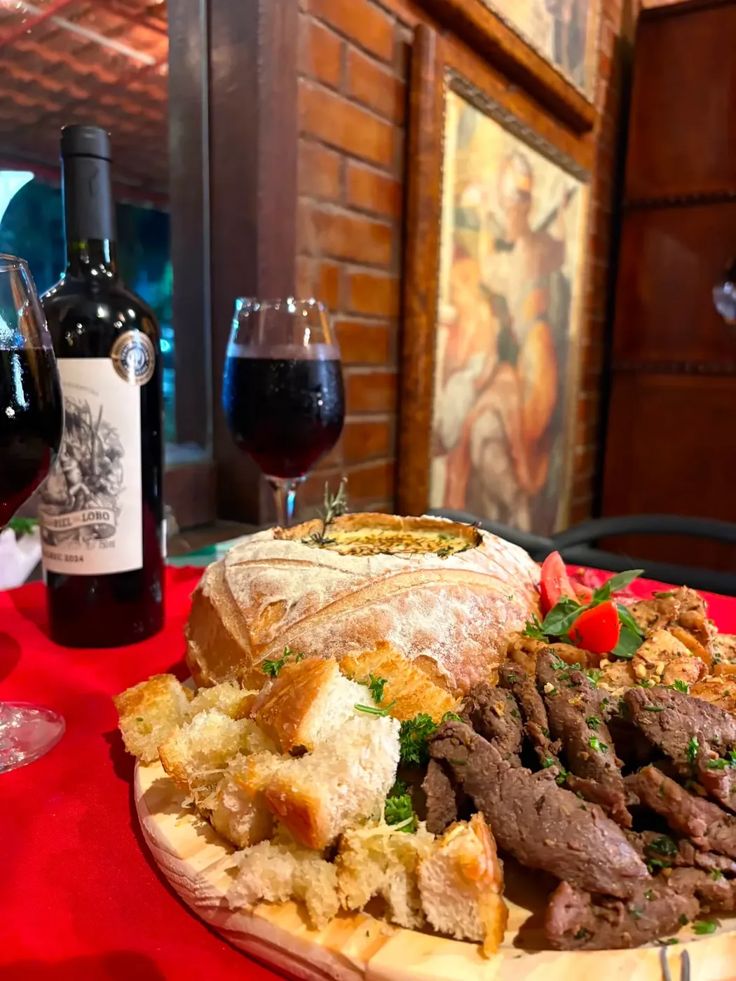 Tábua de carnes com pão e taça de vinho na mesa