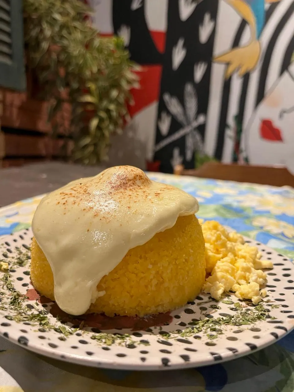 Cuscuz com queijo derretido servido em frente ao mural colorido