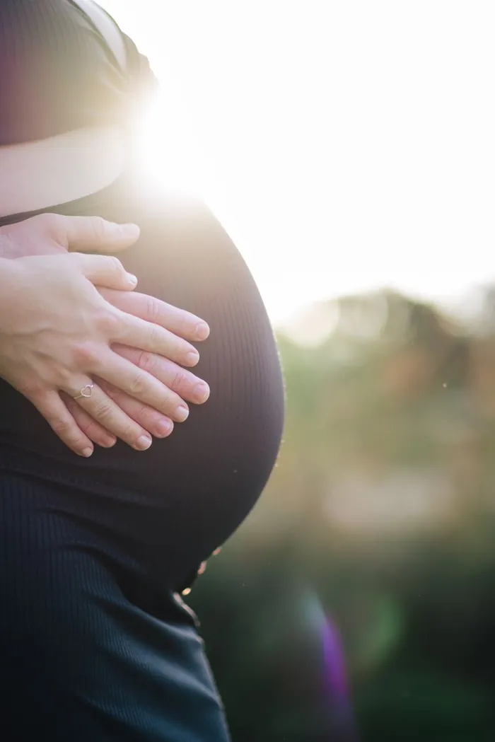 Mulher grávida segurando a barriga ao ar livre, sem o rosto aparecer, representando o salário-maternidade